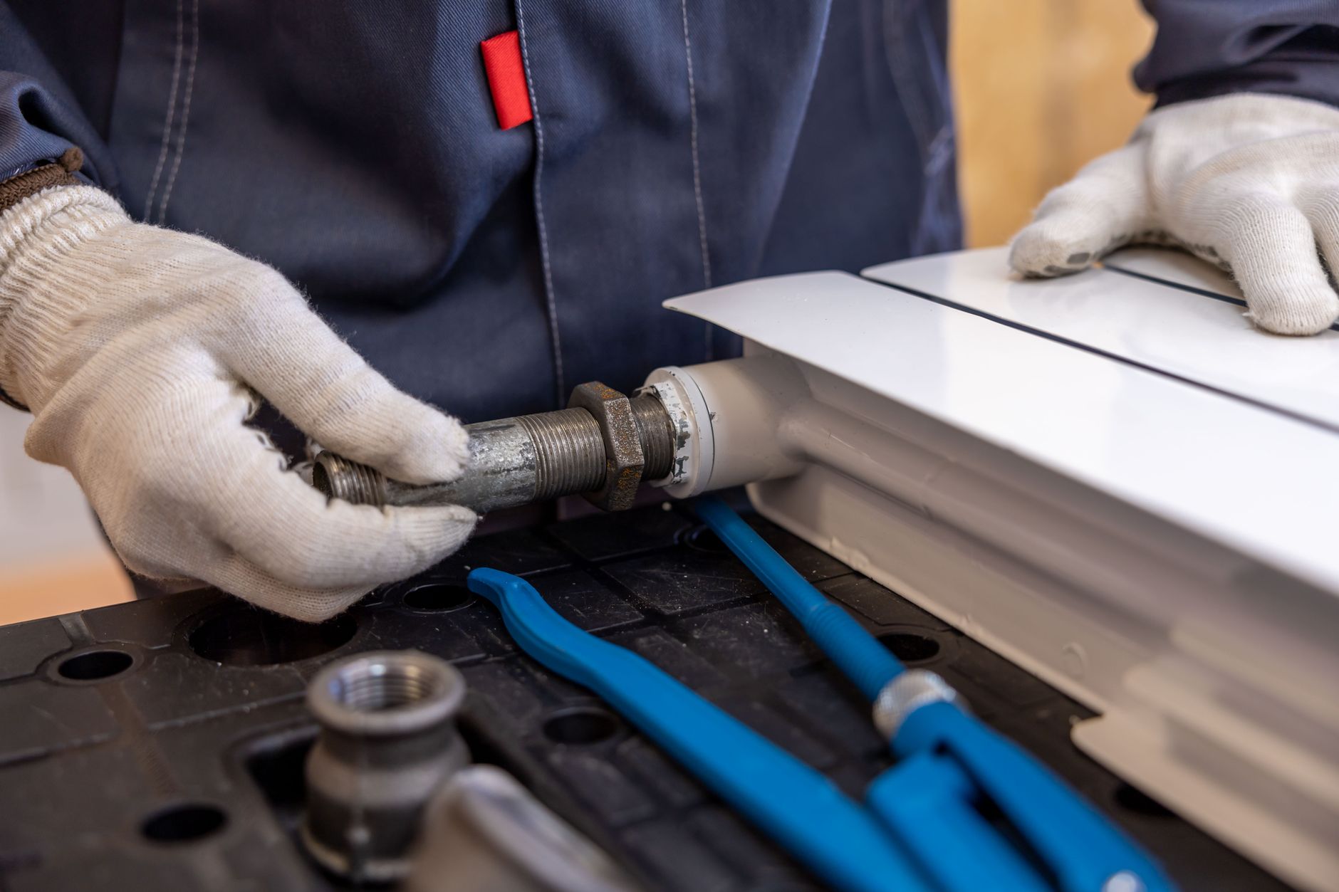 Close-up of gloved hands fitting a threaded pipe connection beside hand tools