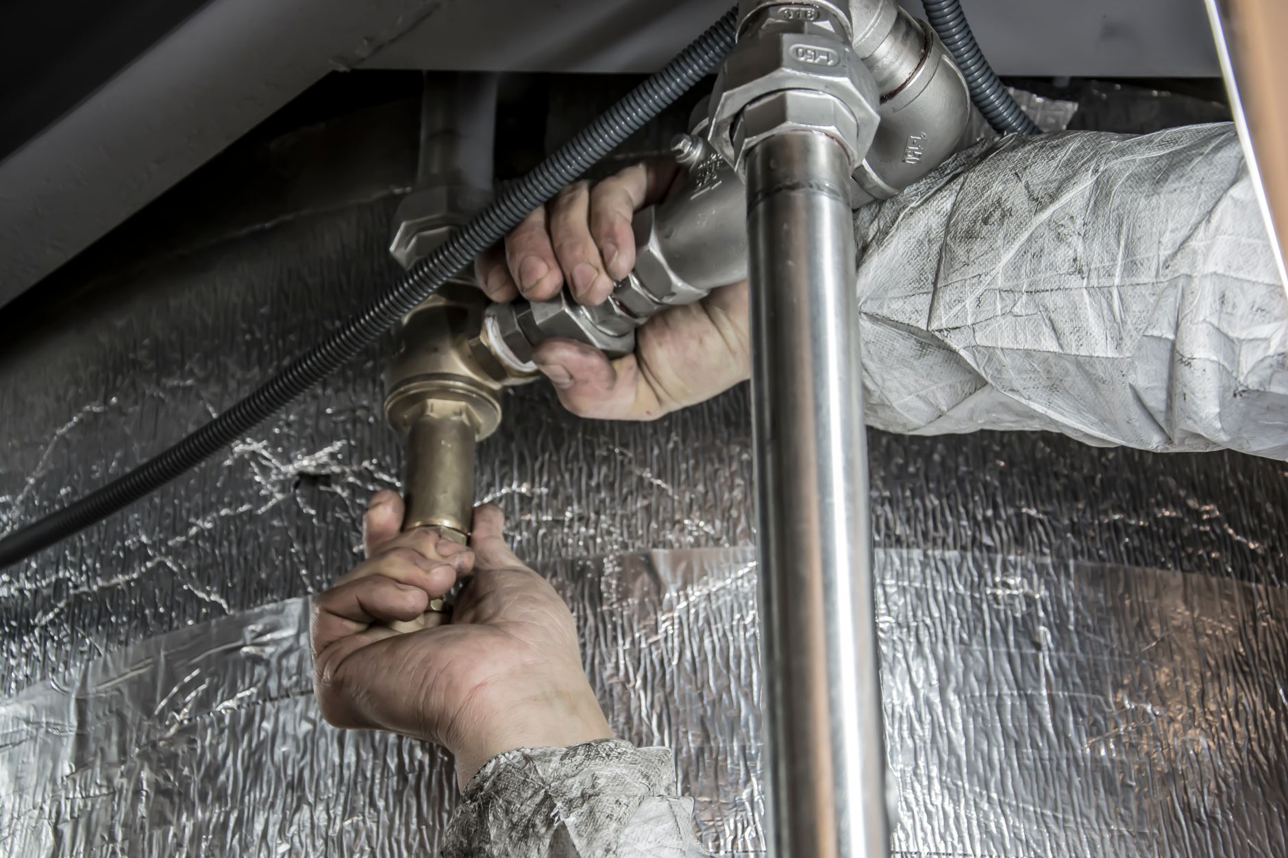 Hands tightening a steel pipe fitting beneath insulation
